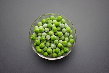 Frozen green peas in a glass bowl on a gray background.