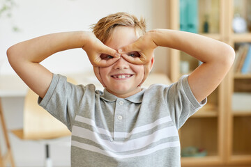 Front view portrait of happy boy making faces at camera pretending to be superhero wearing mask in home interior