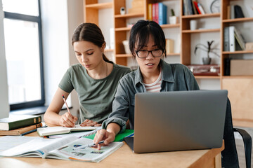Photo of focused multinational students girls doing homework with laptop