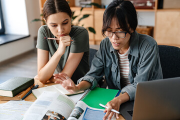 Photo of focused multinational students girls doing homework with laptop