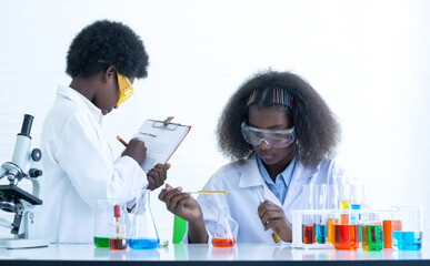 Dark-skinned Boy and girl interested  experimenting with chemistry at the lab, lorem ipsum text on clipboard