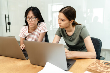 Photo of focused multinational students girls doing homework with laptops
