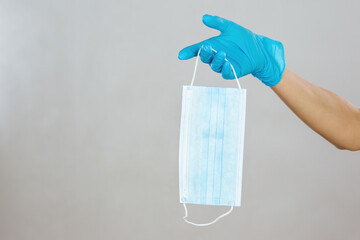Hand in blue rubber gloves holding a surgical mask in studio with copy space. Concept of protection...