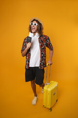 Image of cheerful man in sunglasses posing with passport and suitcase