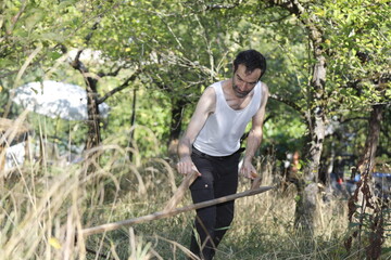 Naklejka na ściany i meble Man with scythe in the garden, grass is mowed and cut by hand.