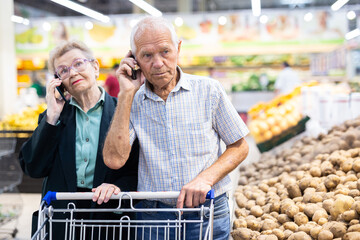 mature european spouses talking on the phone in supermarket
