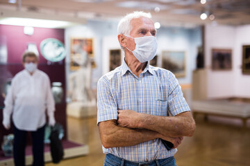 Obraz premium mature man in mask protecting against covid examines paintings on display in hall of art museum