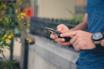mans hands and cellphone reading emails and texting in a garden working from a garden 