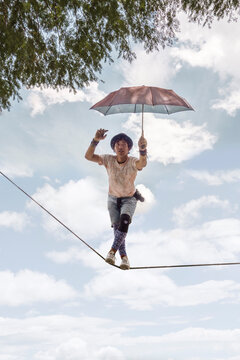 Happy, Talented Tightrope Walker High Up Against Sky, With Umbrella