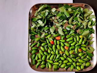 Top view of small green chillies and curry leaves kept in silver plate. Isolated on white...