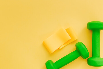 
Dumbbells and fitness elastic band for women lie on yellow background. Healthy lifestyle, female fitness concept. Place for text.