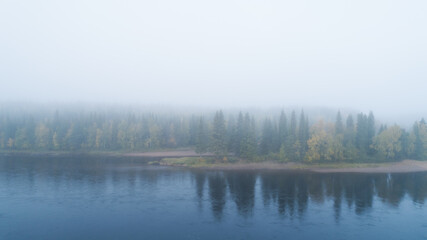 Autumn with mirrored forest and misty Northern river. Morning on the river. Lapland. 