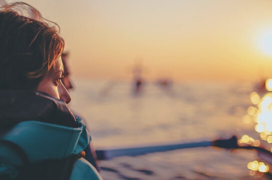 Profile of a young woman sailing on the traditional wooden boat during the sunrise