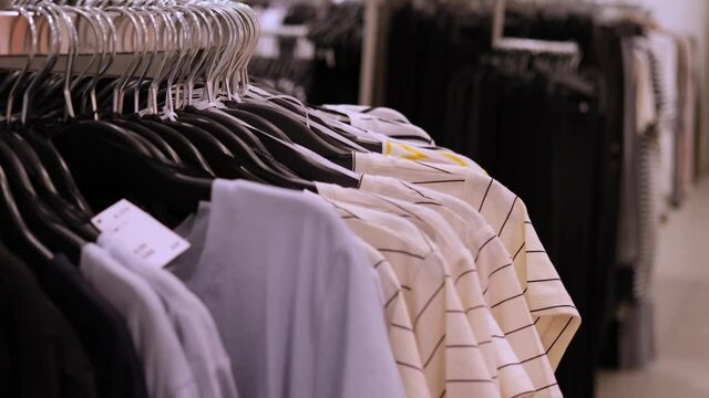 woman makes purchases, goes through a row of identical clothes on hangers in a store, concept of fashion, shopping, seasonal sales, high prices for consumer goods