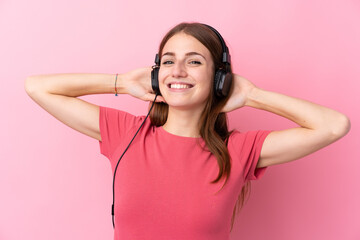 Young woman over isolated pink background listening music