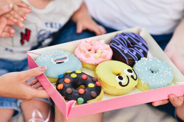 Colored doughnuts in a box on the hands of the family