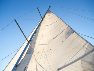 Sailboat mast in the mediterranean sea with blue sky. Vacation, summer and adventure concept. Mainsail unfold in the wind.