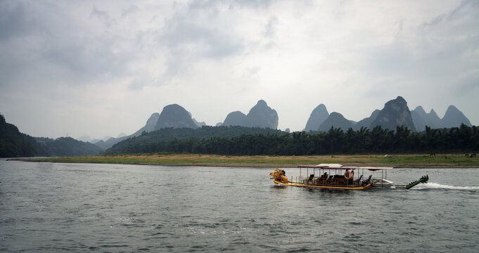 Dragon-like boat on a Lee river with karst formation at the background