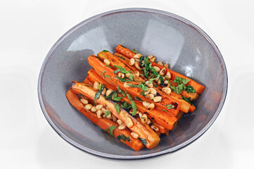 Vegetarian garnish dish of cooked sliced carrots with oil, spices, green herbs and pine nuts