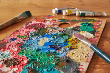 Colorful palette with brushes and oil colors on a wooden table.