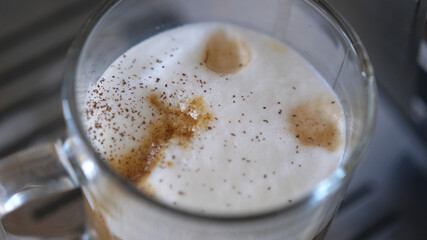 Pouring cinnamon powder into cappuccino coffee cup
