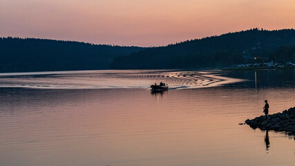Sunset Lake Lipno Czech Risbublika A girl is standing on the shore and a boat is sailing in the distance.