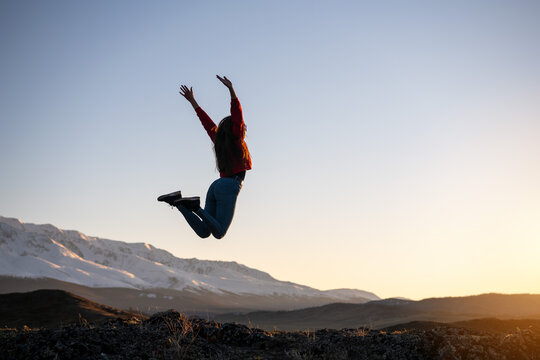 Slim girl jumps against mountains and sunset