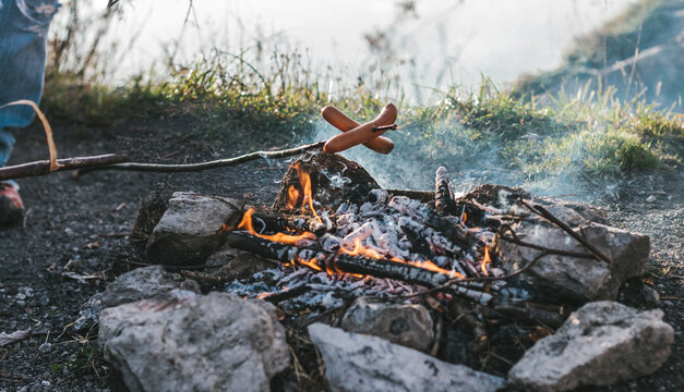 sausages on a wooden stick getting grilled over a camp fire