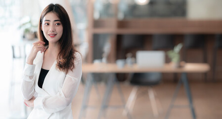 Portrait of young pretty asian businesswoman standing in office, copy space, panoramic view.