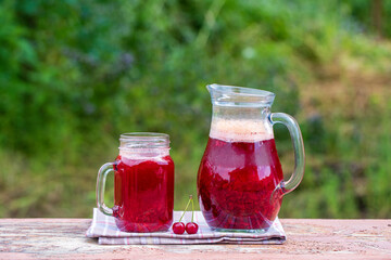 Homemade red cherry drink on the wooden table in garden background