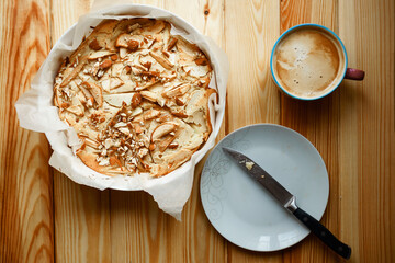 homemade apple pie with cinnamon. cup of coffee, pie and knife on white plate on the wood background 