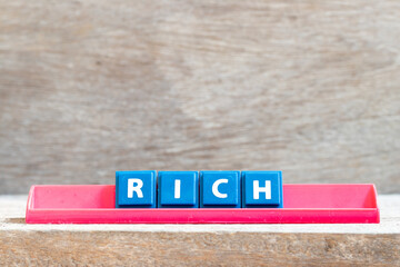 Tile letter on red rack in word rich on wood background