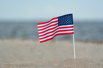 Naklejka premium Flag of United States of America on sandy shore. National flag of America, sea background.