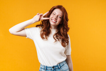 Image of ginger joyful girl winking and gesturing peace sign