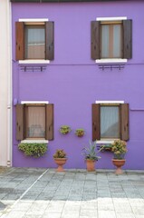 Purple house facade with four open windows and brown shutters, on Burano island near Venice in Italy, closeup, copy space