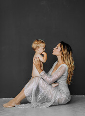 Fototapeta na wymiar Beautiful mother hugs her little son on a gray background.