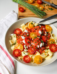 Tomato sauce pasta topped with cherry tomatoes on white plate over a white table. Food styling and photography. 