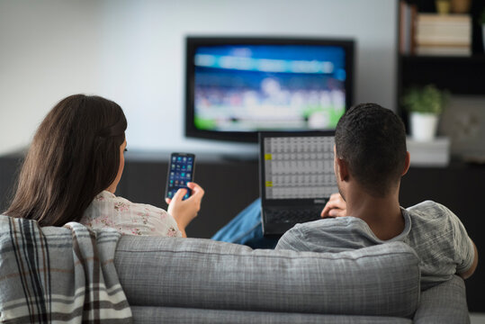 Couple sitting in living room, using laptop and cell phone
