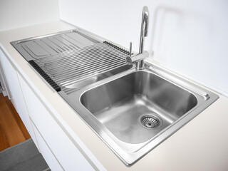 Very clean and lustrous stainless steel kitchen sink. Stainless steel drainer board over the sink.