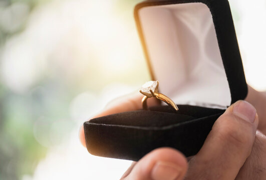 Close up of man's hand holding open box with engagement ring