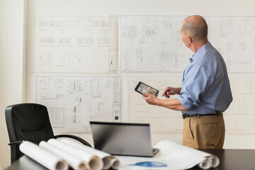 Mature architect looking at blueprints in office
