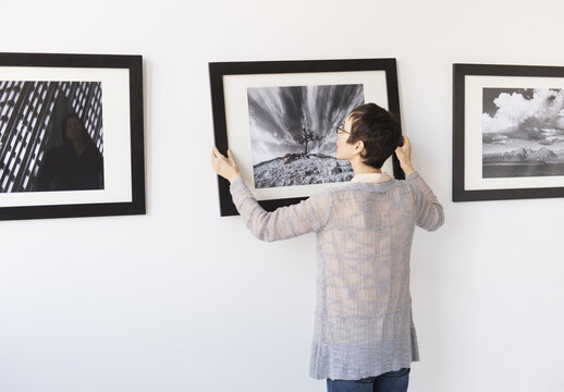 Woman hanging photographs in art gallery