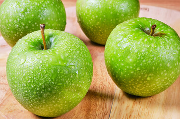 Four green apples in drops of water on a wooden Board.