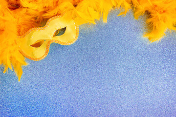 Yellow carnival mask and feather boa on blue texture background with copy space. Blank for a holiday cardon on mardi gras, congratulations. Photo for a theater poster or children's acting school.