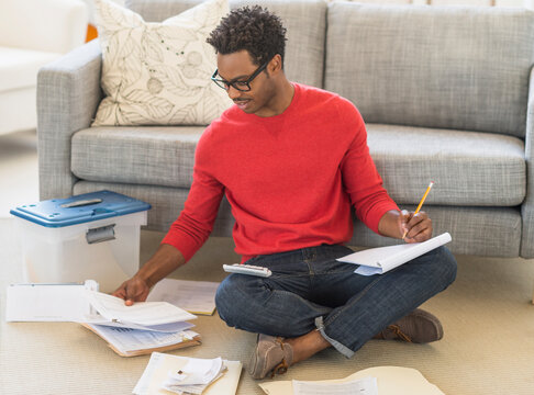 Man sitting on floor in living room and calculating bills