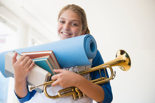 Portrait of teenage girl (12-13) holding rolled-up exercise mat, books, and trumpet