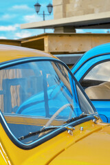 Car hood and windshield of a yellow car on the background of a blue car close-up.