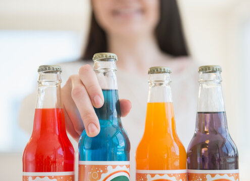 Young woman reaching for colorful bottles of soda