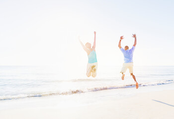 Mature couple jumping in sea with arms raised