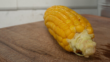 Delicious corn on the cob that's just been boiled is laying on a wooden board.
The brightly glowing yellow kernels form a recognizable pattern. The cob was seasoned with salt and hot spices.
